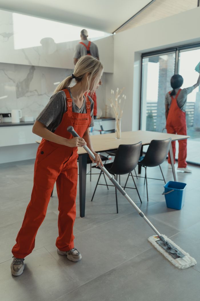 about-us Cleaning team in red overalls mopping and sanitizing a modern home interior.